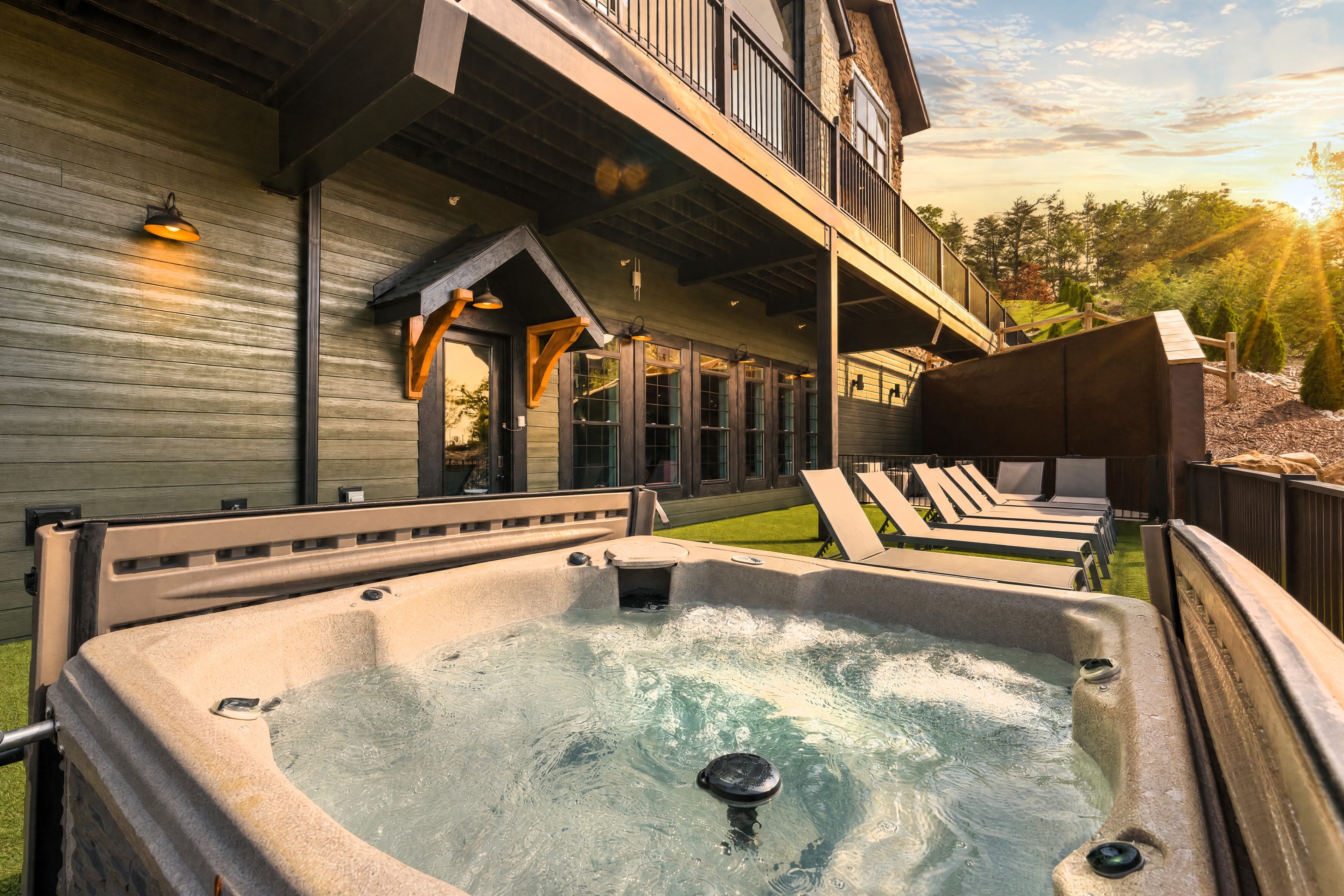 Excalibur hot tub bubbling at golden sunset with lodge exterior, lounge chairs, and pergola