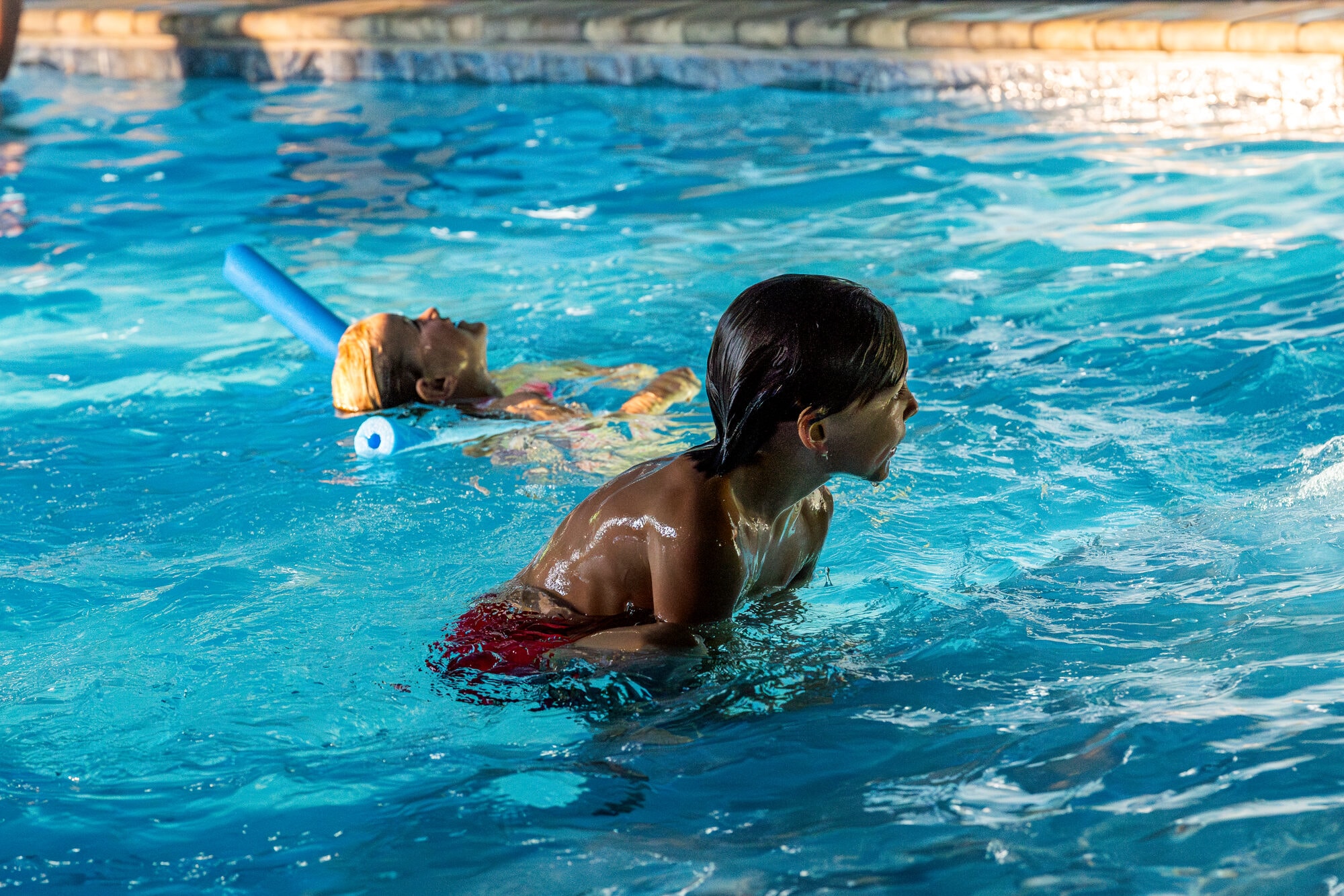 Kids swimming in Excalibur's heated indoor pool pool noodle golden light