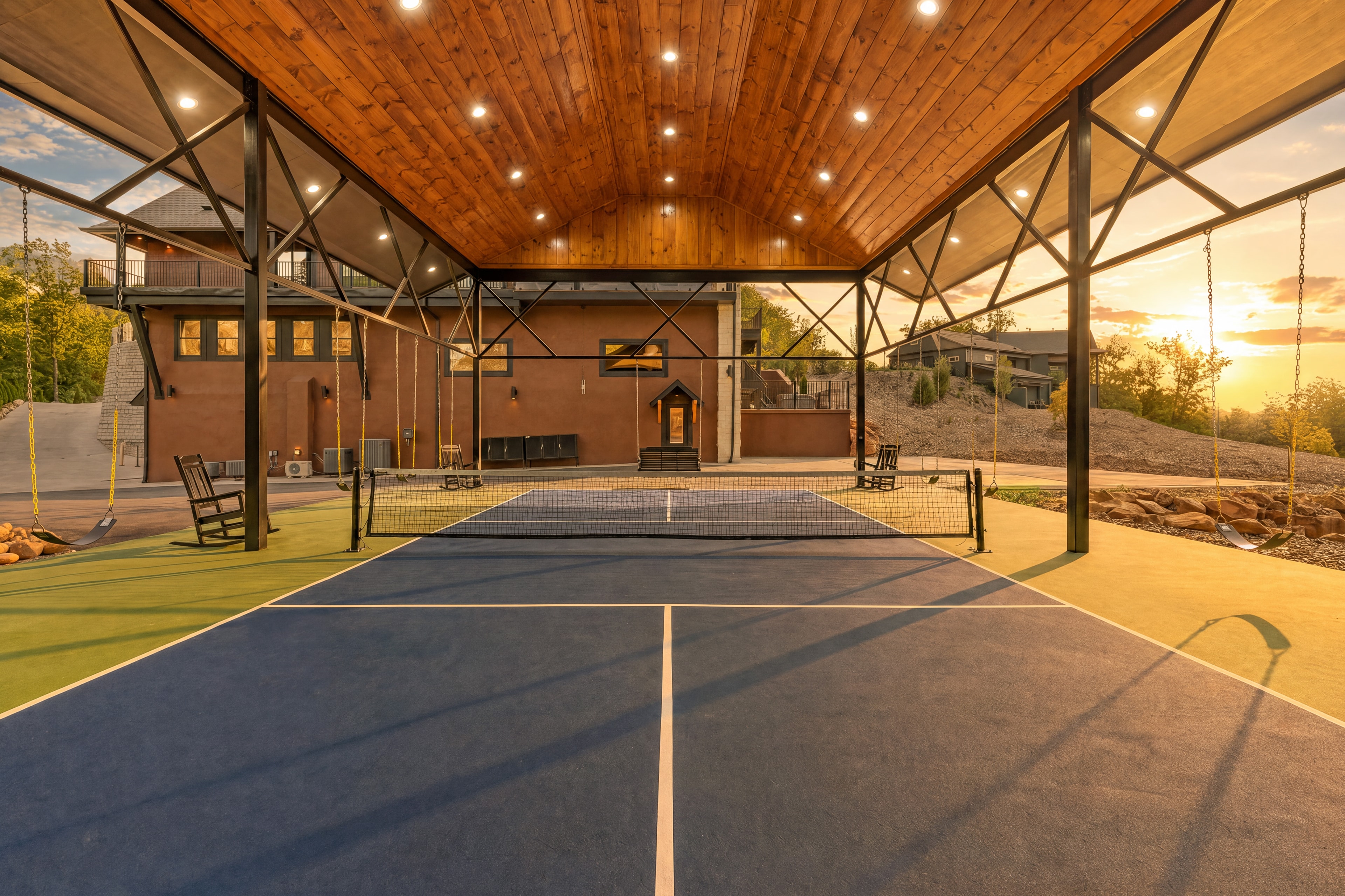 Excalibur covered pickleball court from inside — wooden ceiling, net, rocking chairs, golden sunset through open sides